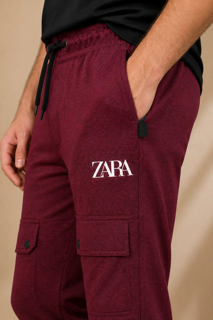 A close-up of a person wearing heather burgundy cargo jogger pants with a white ZARA logo on the left thigh, a black drawstring waist, and side cargo pockets.