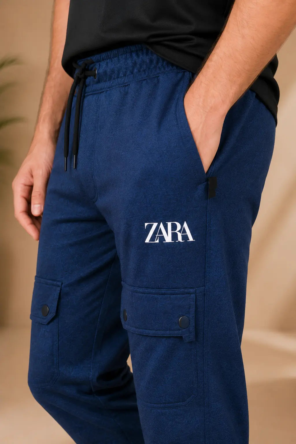 A close-up of a person wearing navy blue jogger-style cargo pants with a white embroidered ZARA logo on the left thigh, a black drawstring waist, and side pockets.